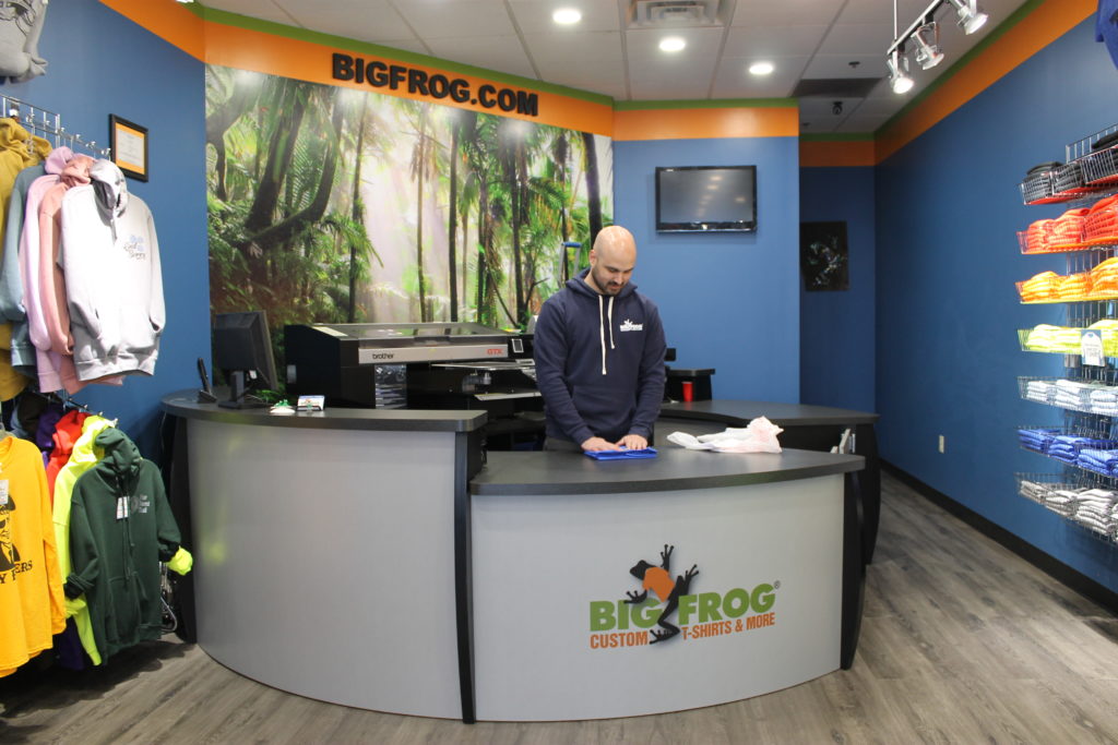 A Man Standing At A Counter In A Big Frog Franchise Store.